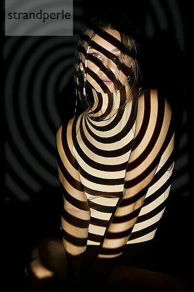 Junge Frau mit beleuchtetem Spiralmuster vor schwarzem Hintergrund