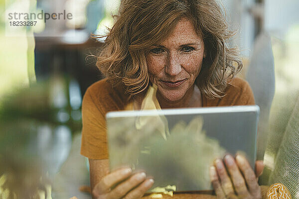 Reife Frau mit Tablet-PC durch Glasfenster gesehen