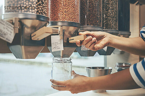 Hände einer Frau halten Einmachglas unter Lebensmittelspender im Geschäft