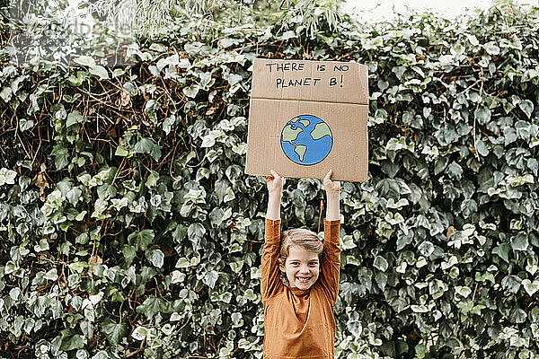 Glückliches Mädchen mit erhobenen Armen  das ein Banner mit Botschaft und Planetenzeichnung vor der Pflanze hält