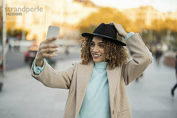 Lächelnde Frau mit Hut macht ein Selfie mit dem Handy