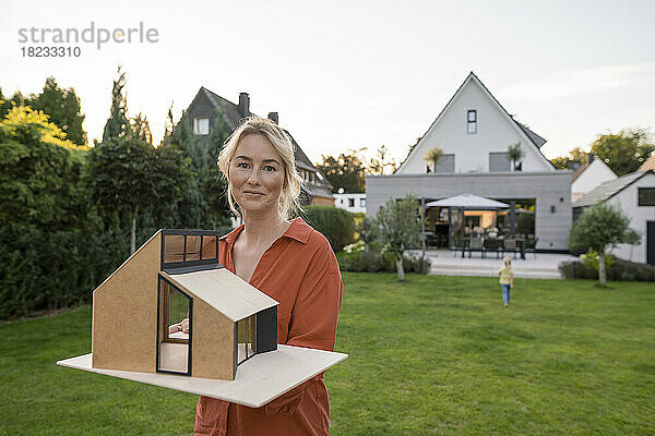 Lächelnde Frau hält Musterhaus im Garten