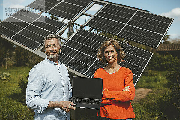 Lächelnder Mann und Frau mit Laptop vor Sonnenkollektoren an einem sonnigen Tag
