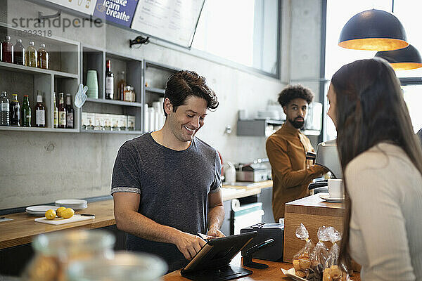 Lächelnder Barista mit Tablet-PC an der Theke im Café