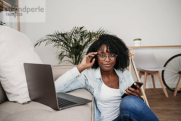 Geschäftsfrau mit Smartphone und Laptop auf dem heimischen Sofa