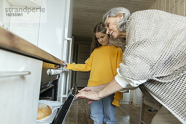 Großmutter und Enkelin holen frisch gebackenes  selbstgebackenes Brot aus dem Ofen