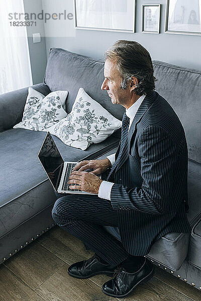 Nachdenklicher Geschäftsmann mit Laptop auf dem Sofa  der zu Hause arbeitet