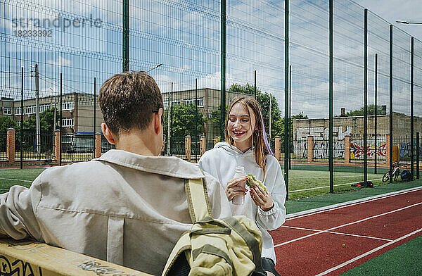 Lächelndes Mädchen isst Sandwich mit Freund auf dem Schulhof