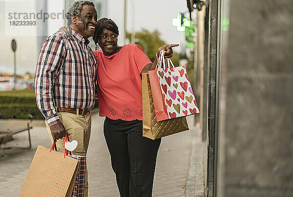 Aufgeregte Frau mit Einkaufstüten zeigt Mann auf Laden