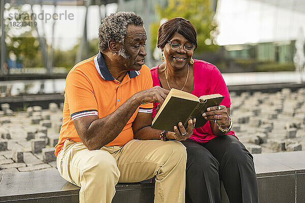Älteres Paar liest ein Buch und sitzt an der Wand