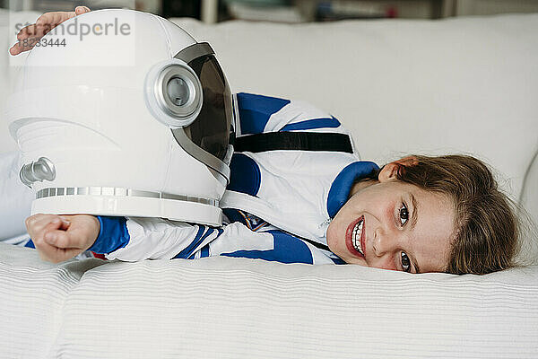 Smiling girl wearing space costume lying on sofa at home