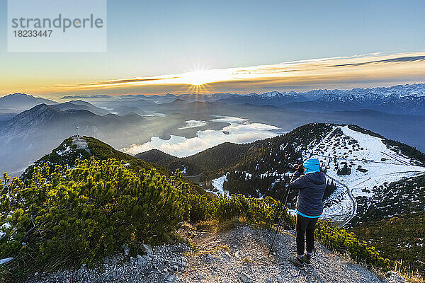 Germany  Bavaria  Woman photographing surrounding landscape from summit of Herzogstand mountain at sunrise