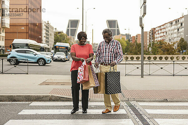 Glückliches Paar überquert mit Einkaufstüten die Straße in der Stadt
