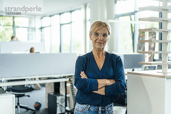 Selbstbewusste Geschäftsfrau mit Brille und verschränkten Armen im Büro