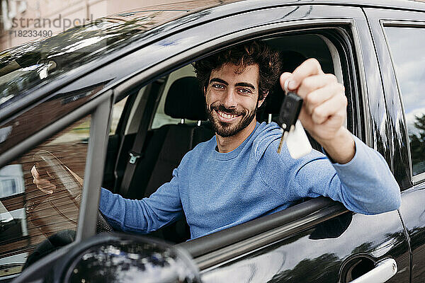 Lächelnder Mann mit Schlüssel im Auto sitzend