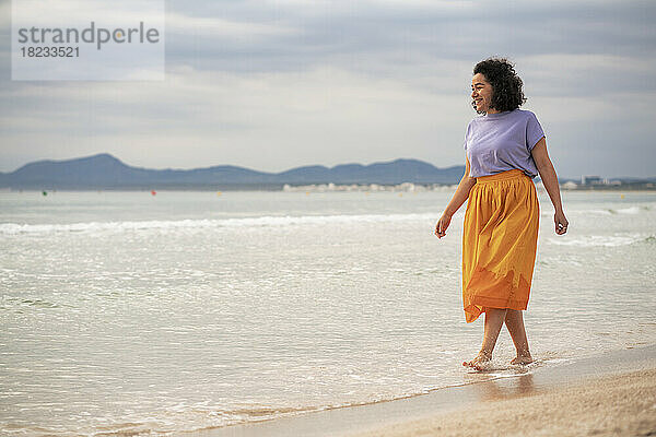 Lächelnde Frau  die bei Sonnenuntergang am Strand spaziert