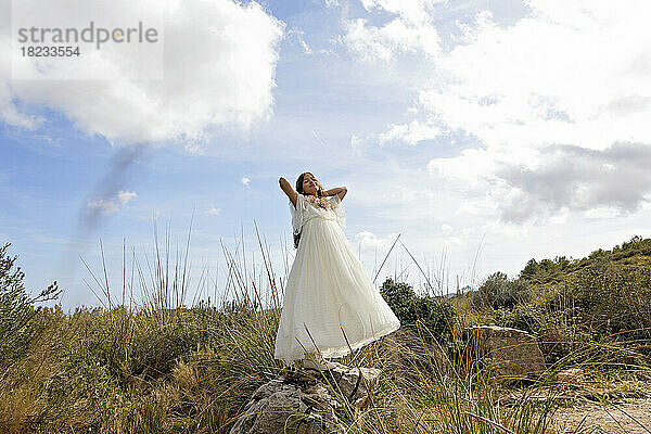 Lächelndes Mädchen in weißem Kleid  das auf einem Felsen steht