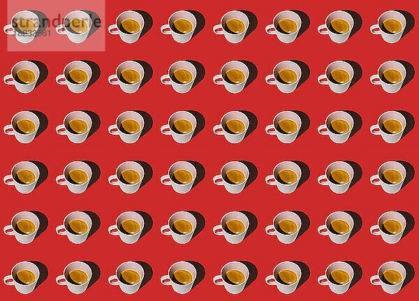 Muster aus in Reihen stehenden Tassen Kaffee vor rotem Hintergrund