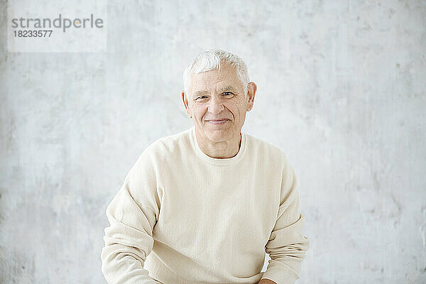 Lächelnder älterer Mann vor der Wand zu Hause