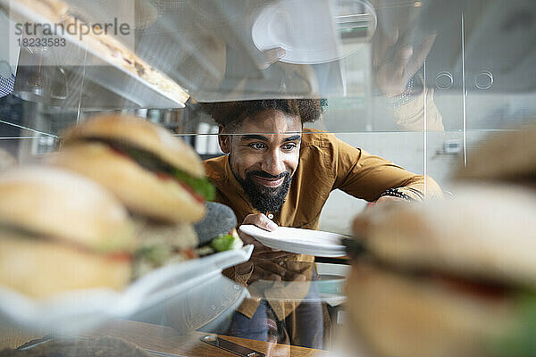 Lächelnder Cafébesitzer  der Burger aus der Vitrine im Café holt