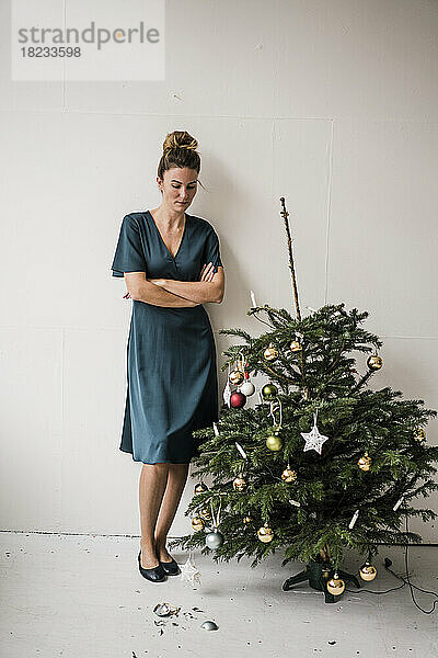 Frau steht mit verschränkten Armen und blickt auf eine zerbrochene Christbaumkugel vor einer weißen Wand