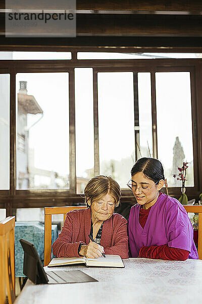 Gesundheitshelfer mit älterer Frau  die am Tisch Tagebuch schreibt