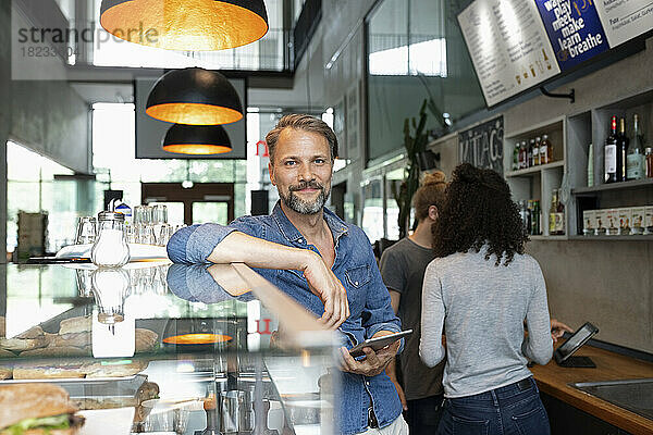 Lächelnder Cafébesitzer steht mit Tablet-PC im Café