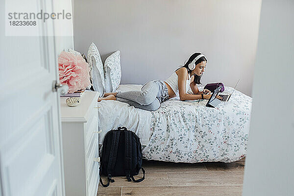 Mädchen mit Kopfhörern liegt auf dem Bett und nutzt zu Hause drahtlose Technologien