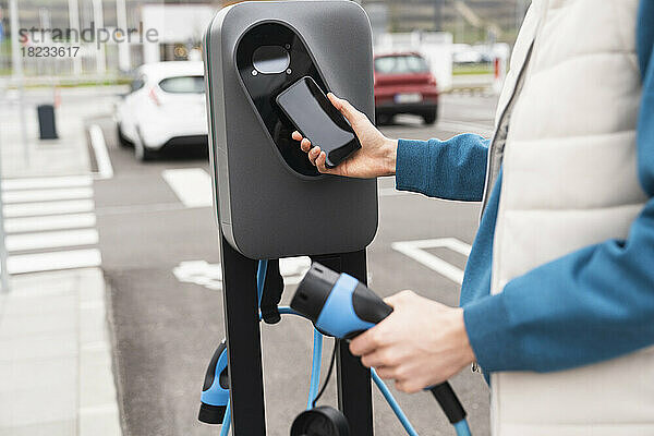 Mann scannt und bezahlt per Smartphone an der Ladestation