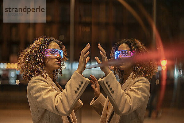 Frau mit Smart-Brille berührt ihr Spiegelbild an einer Glaswand