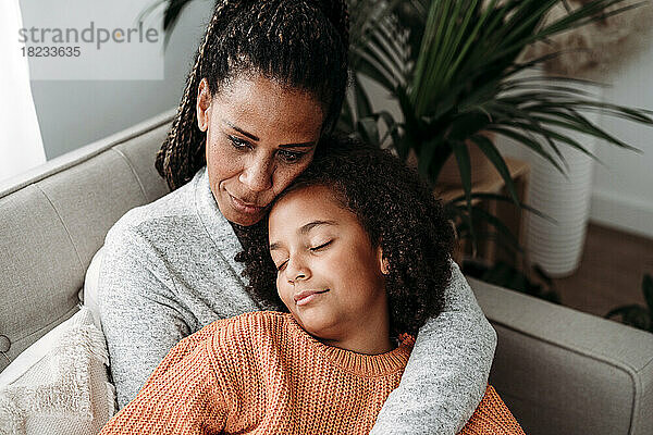 Mutter umarmt Tochter und entspannt sich zu Hause auf dem Sofa
