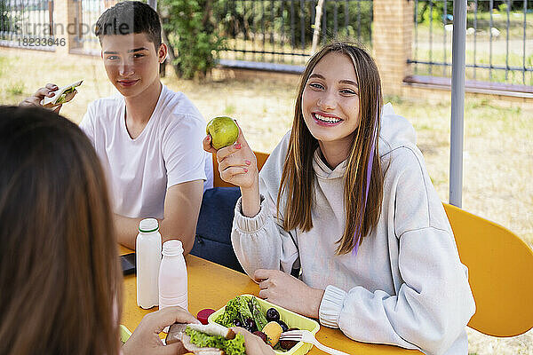 Happy girl having fresh fruit sitting at table in schoolyard