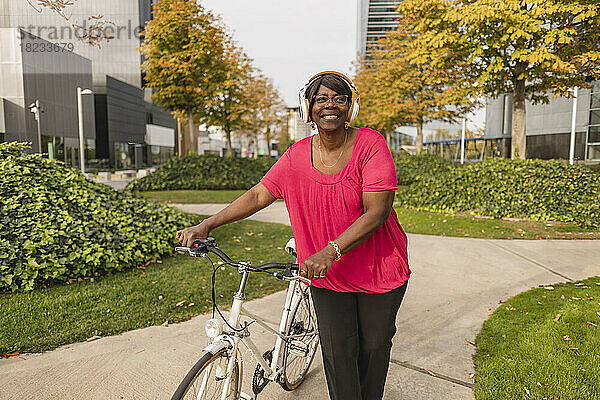 Lächelnde ältere Frau mit Kopfhörern  die im Park Fahrrad fährt