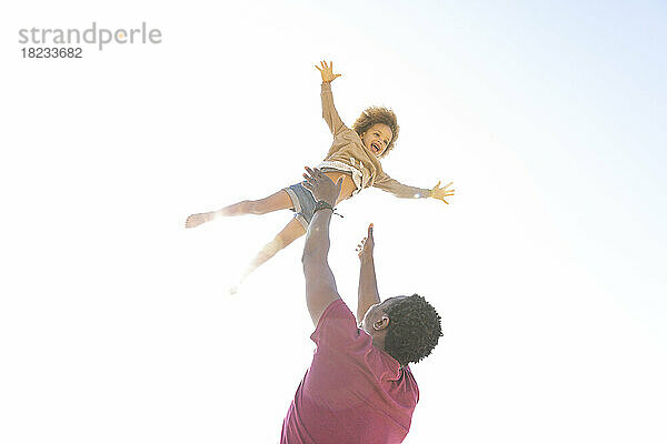 Verspielter Vater hat Spaß mit seiner Tochter unter klarem Himmel an einem sonnigen Tag