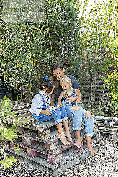 Familie mit Buch sitzt auf Holzpalette