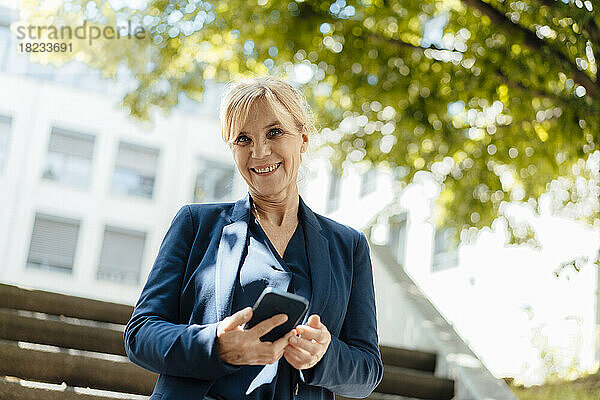 Glückliche Geschäftsfrau mit Smartphone an einem sonnigen Tag