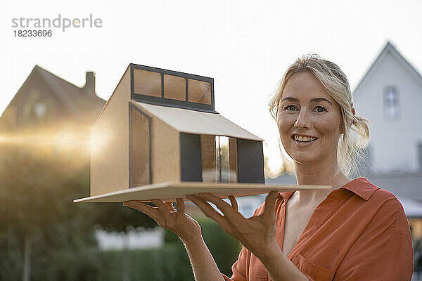 Smiling woman with blond hair holding model house
