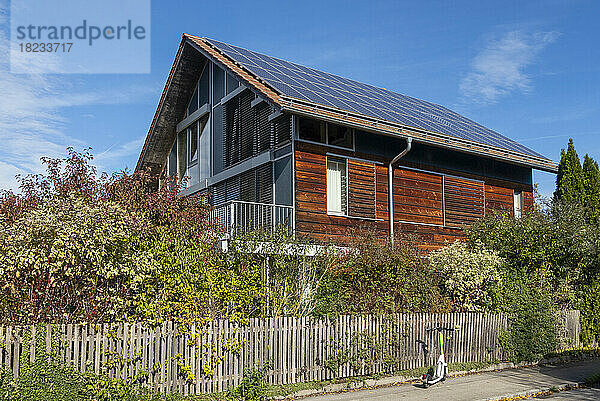 Deutschland  Bayern  München  Elektroroller links vor einem modernen Passivhaus mit Sonnenkollektoren
