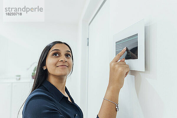 Lächelnde Frau benutzt Smart-Home-Gerät an der Wand