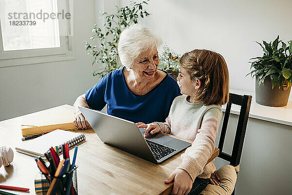 Glückliches Mädchen mit Laptop auf dem Tisch und Blick auf die Großmutter