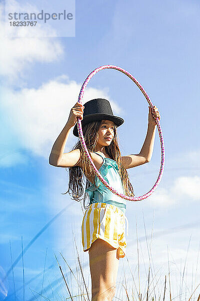 Girl wearing hat holding plastic hoop under sky