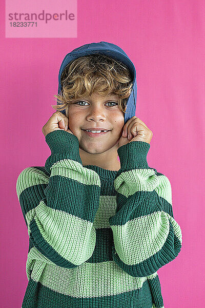 Smiling boy wearing striped sweater against pink background