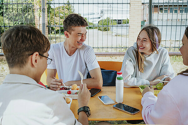Glückliche Teenager-Freunde  die am Tisch auf dem Schulhof zu Mittag essen