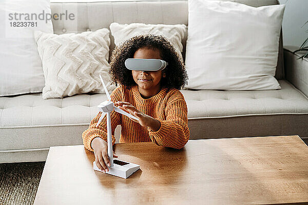 Mädchen mit Virtual-Reality-Simulator sitzt mit Windturbinenmodell im heimischen Wohnzimmer