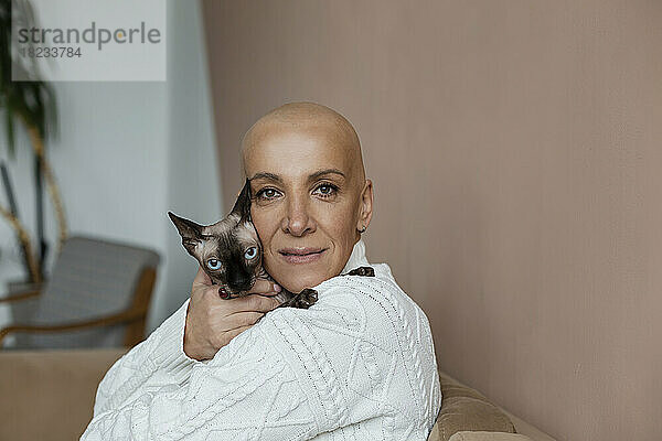 Reife  haarlose Frau umarmt Sphynx-Katze auf dem Sofa