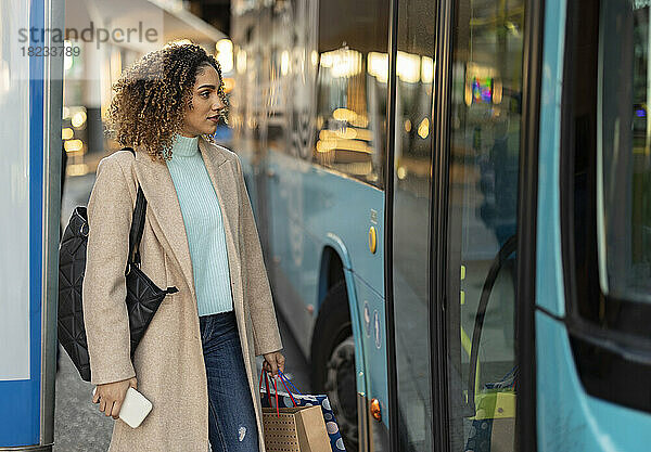 Frau mit Handy und Einkaufstüten steht am Bus