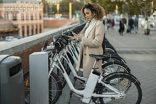 Frau mietet Elektrofahrrad per Smartphone am Parkplatz