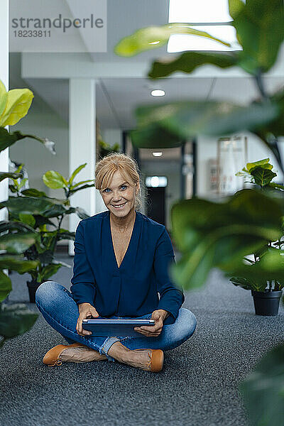 Lächelnde Geschäftsfrau mit Tablet-Computer sitzt am Arbeitsplatz