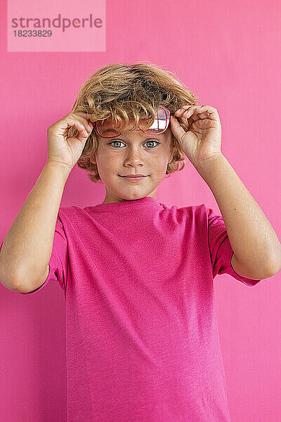 Junge trägt rosa T-Shirt vor farbigem Hintergrund