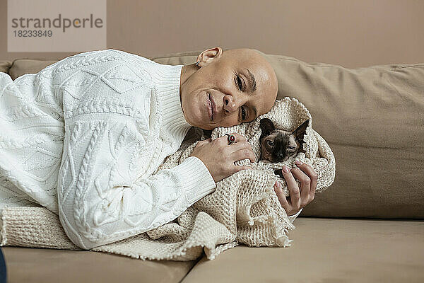 Frau mit Glatze umarmt in Decke gehüllte Sphynx-Katze auf Sofa